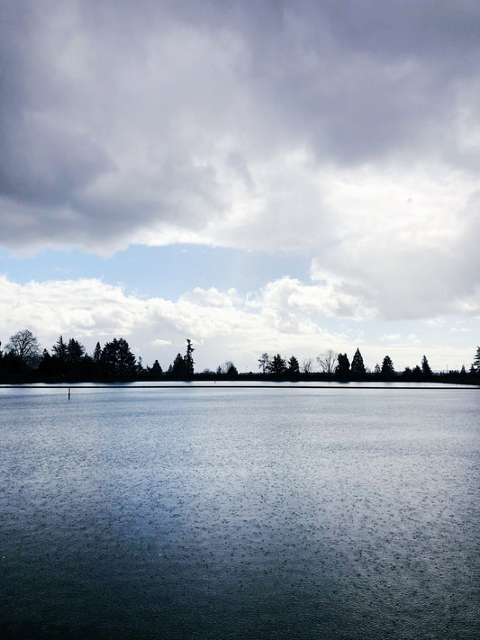 A look across Mt. Tabor reservoir on a stormy day with rain bouncing off the water and clouds above. Blue sky is peeking through the clouds.